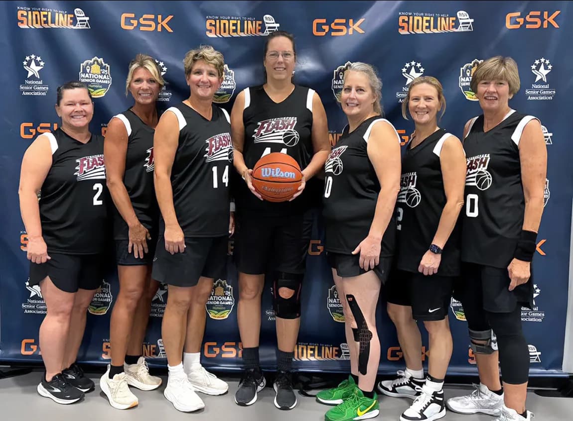 A women's basketball team poses for a picture in front of a branded backdrop.
